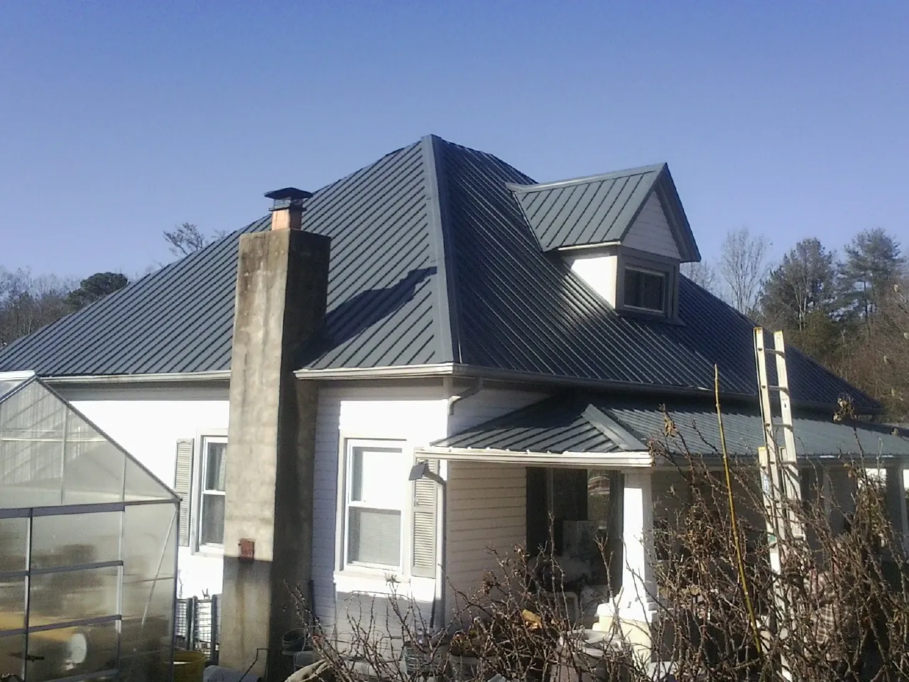 Dark blue standing seam metal roof on a white farmhouse with dormer — Slate & Tile Roof Repair by Roofing Brothers in Fort Lupton