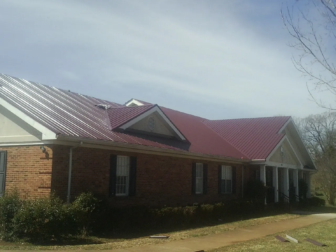 Red metal roof with gabled entries on a long brick building, from a Hail Damage Roof Repair job in Fort Lupton