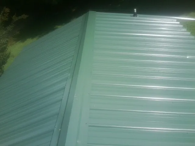 New green metal panels meeting at the ridge of a roof — Flat Roof Repair work by our crew in Fort Lupton