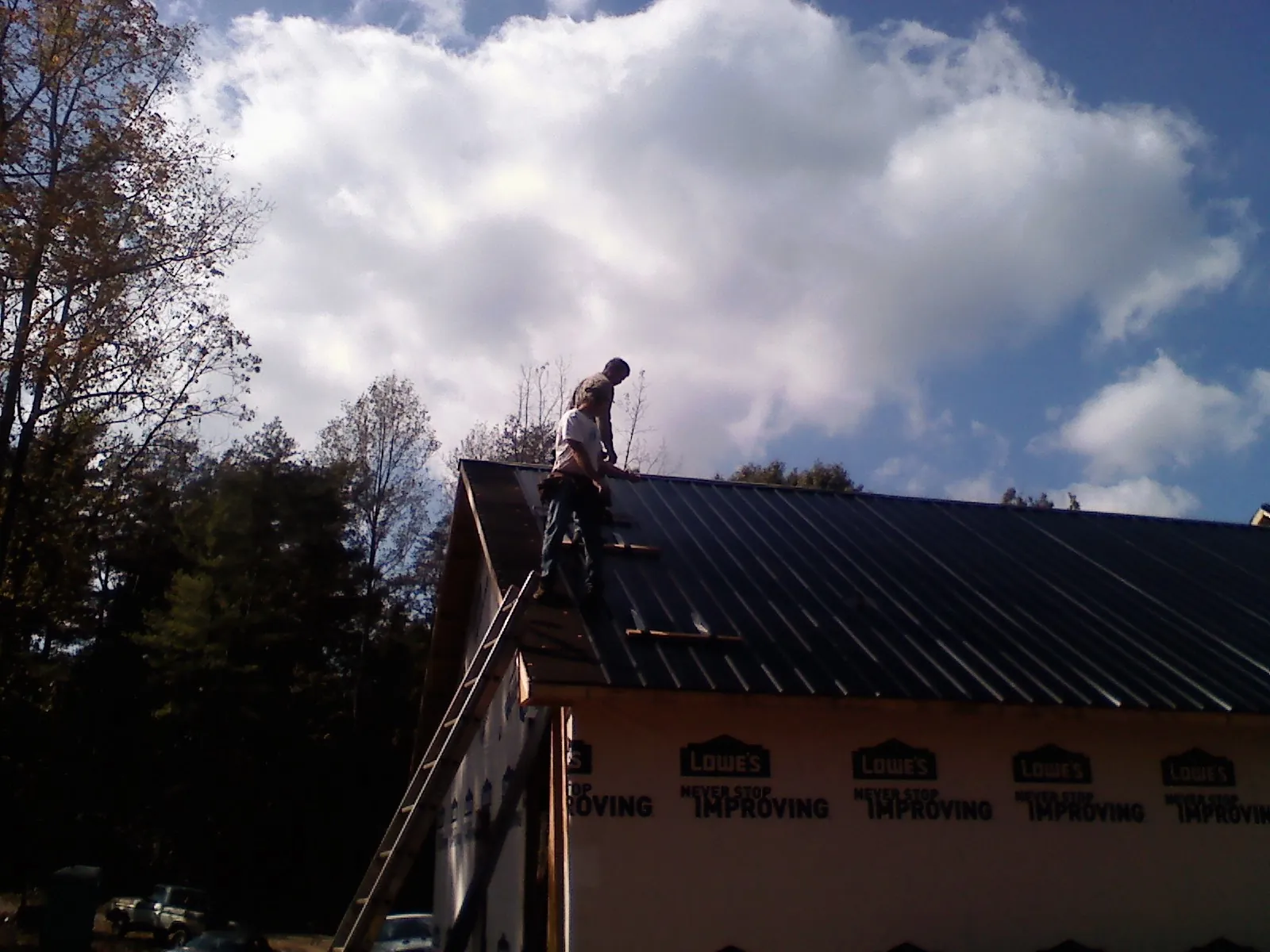 Roofer fastening dark metal panels high against a cloudy sky, from a Roof Inspection job in Fort Lupton
