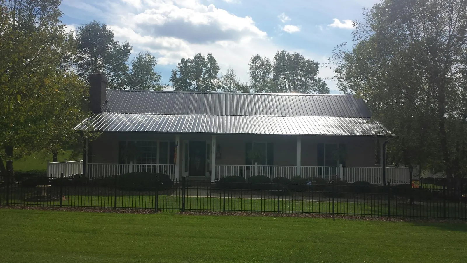 Gray metal roof on a brick ranch with a full width front porch — Gutter Guard Installation work by our crew in Fort Lupton