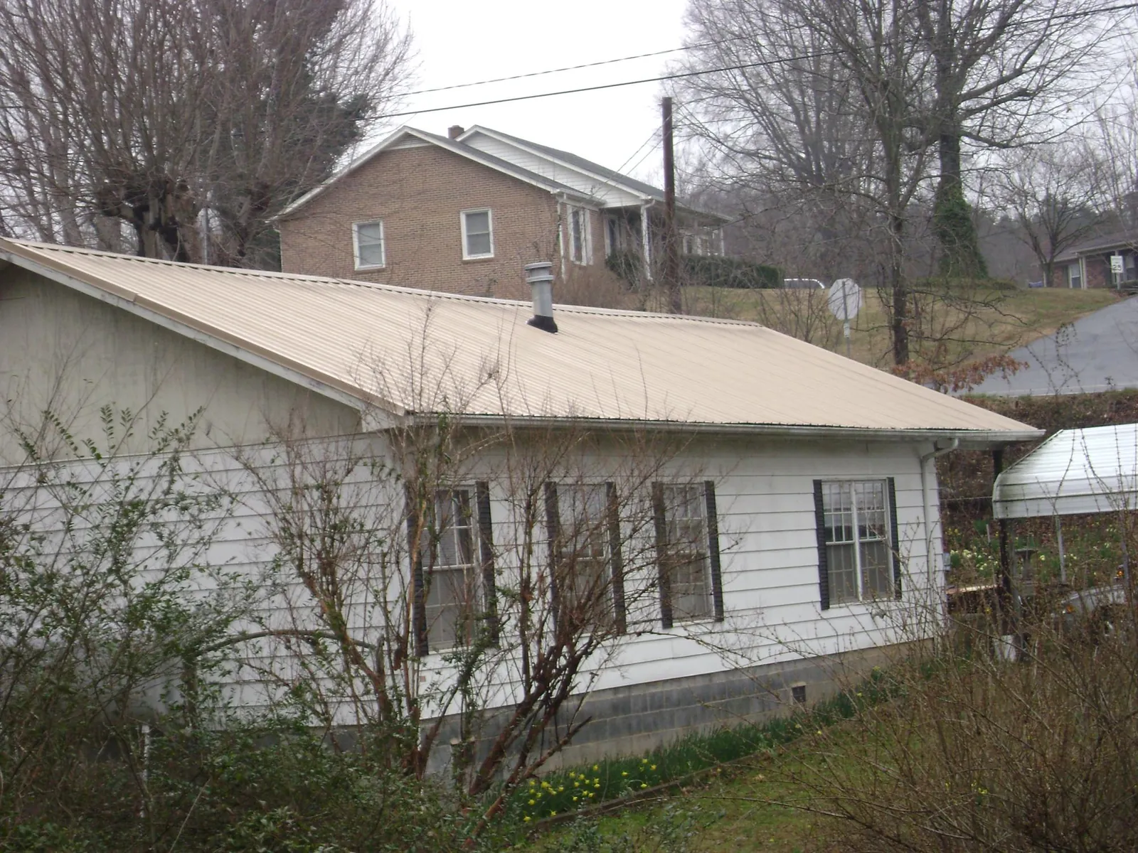 Tan metal roof on a white sided house set into a hillside — Commercial Roofing by Roofing Brothers in Fort Lupton